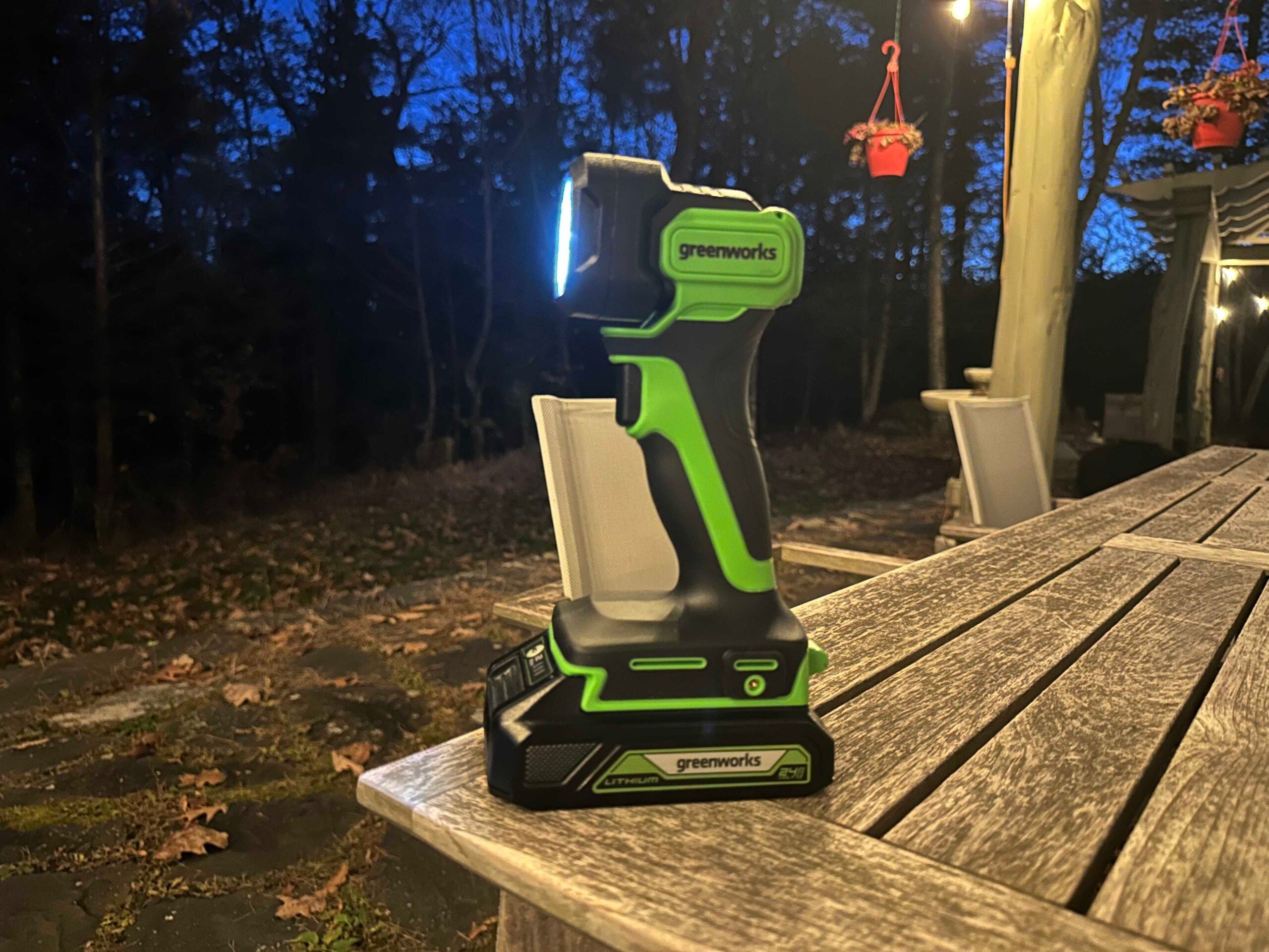 A green and black Greenworks 24V Cordless LED Flashlight outside at night on a table