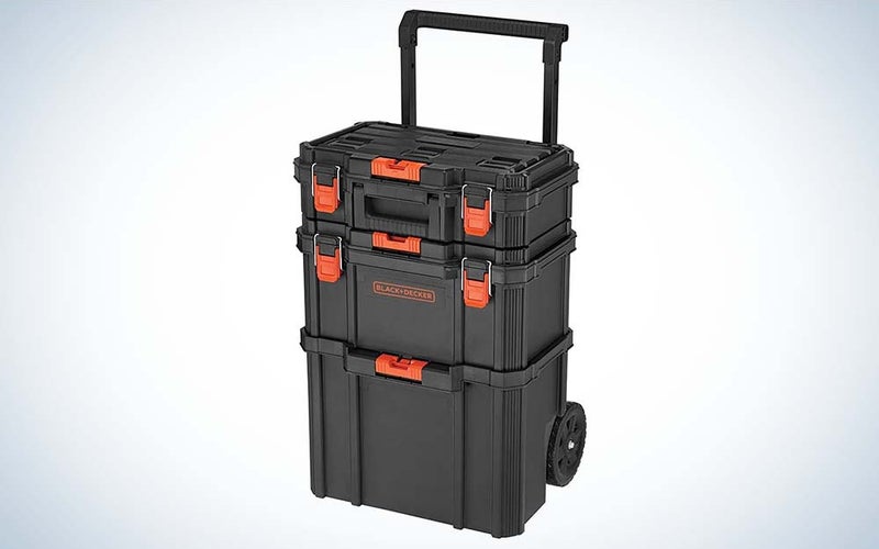 A stack of three black tool storage cases with orange clasps and handles stacked on a black wheeled cart.