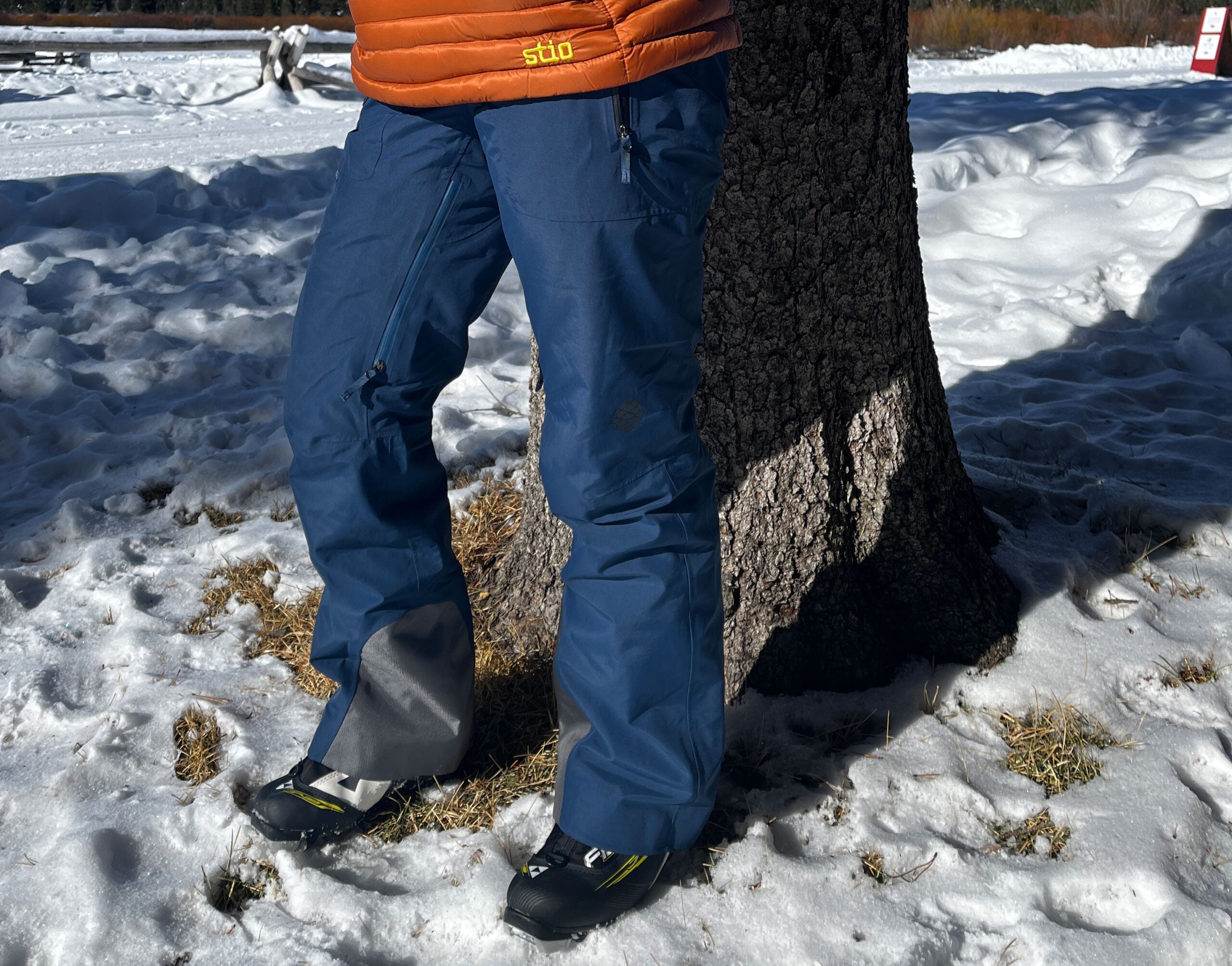A person wearing Stio women's snow pants in front of a tree with snow on the ground