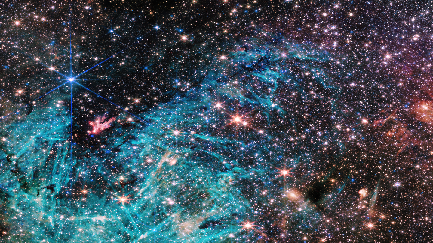 The full view of the James Webb Space Telescope’s NIRCam (Near-Infrared Camera) instrument reveals a 50 light-years-wide portion of the Milky Way’s dense center. An estimated 500,000 stars shine in this image of the Sagittarius C region, along with some as-yet unidentified features. A vast region of ionized hydrogen, shown in cyan, wraps around an infrared-dark cloud, which is so dense that it blocks the light from distant stars behind it. Intriguing needle-like structures in the ionized hydrogen emission lack any uniform orientation. Researchers note the surprising extent of the ionized region, covering about 25 light-years.